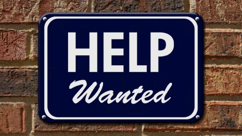 A job ad sign on a brick wall saying "help wanted"
